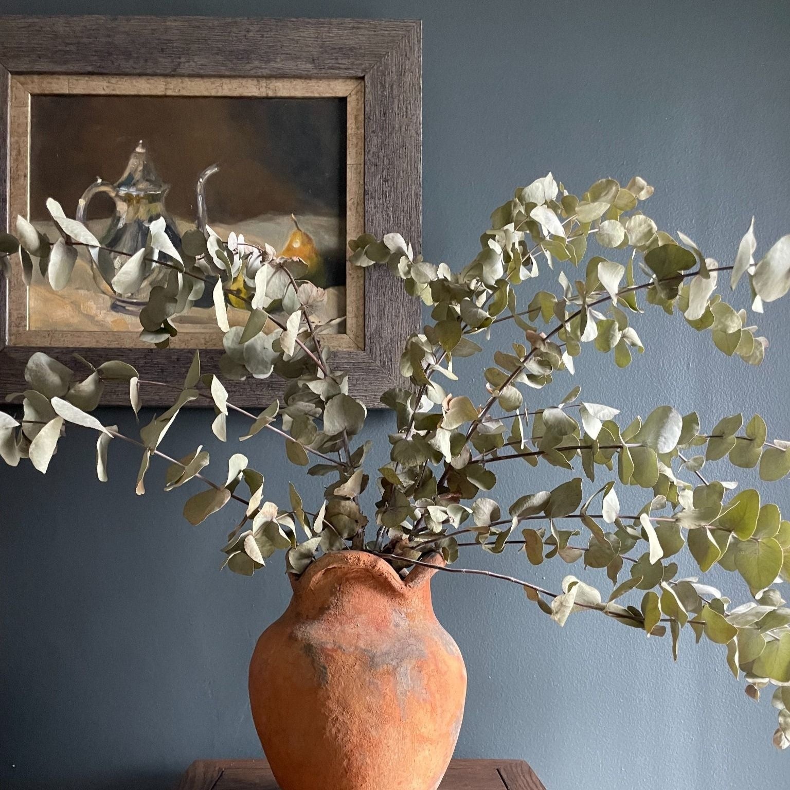 Beautiful oil painting of a silver coffee pot styled next to two pears on a tablecloth, framed in gold edging and a wooden frame.
