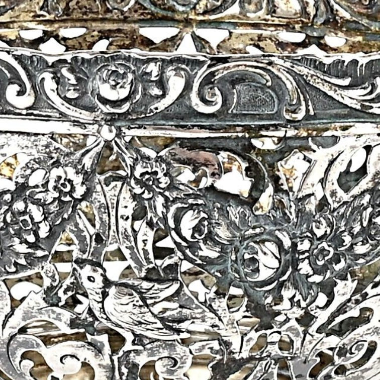 Close-up of intricate silver filigree with floral and bird designs.