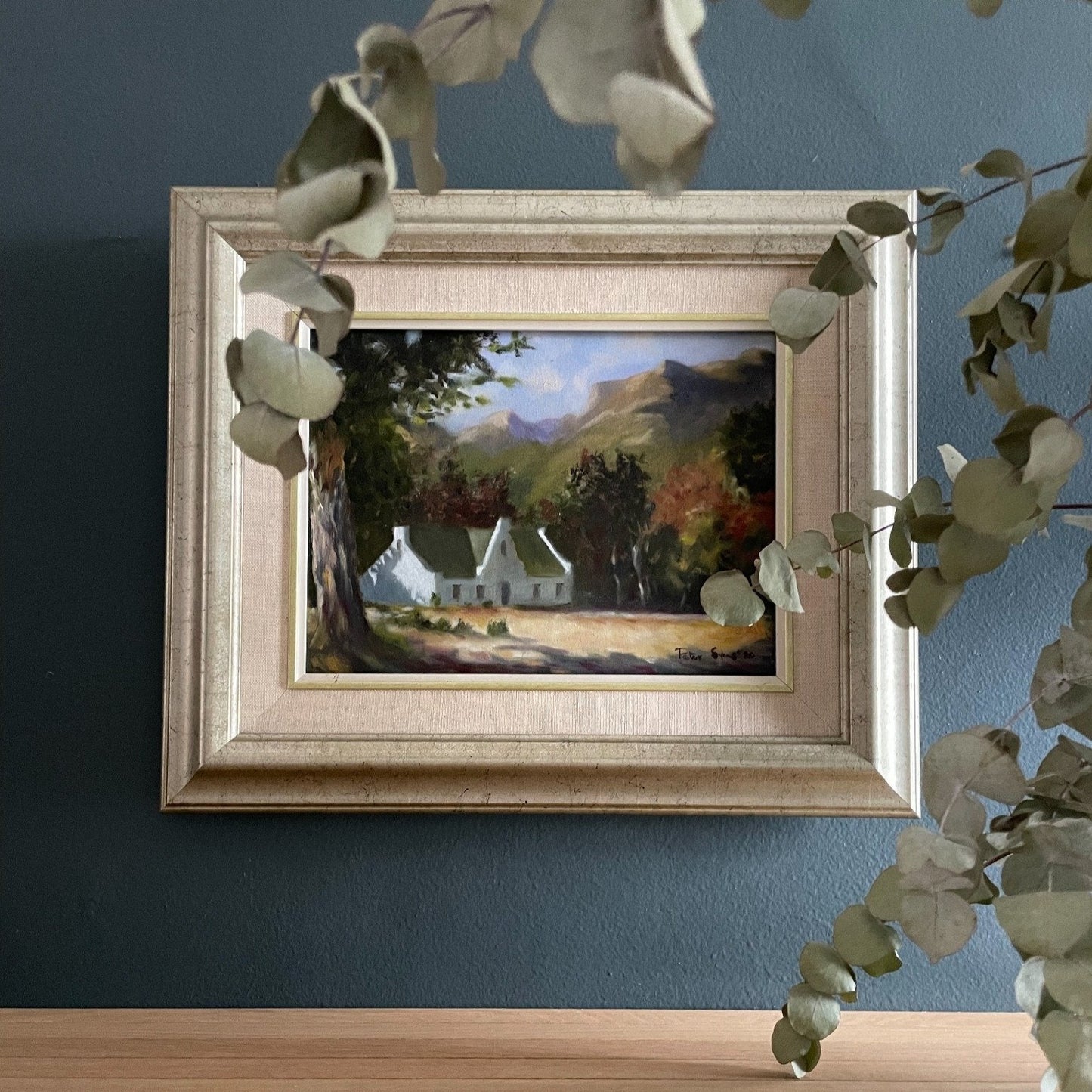 Bathed in soft morning light, this oil painting captures the quiet elegance of a Cape Dutch homestead nestled beneath towering oaks and distant mountain slopes