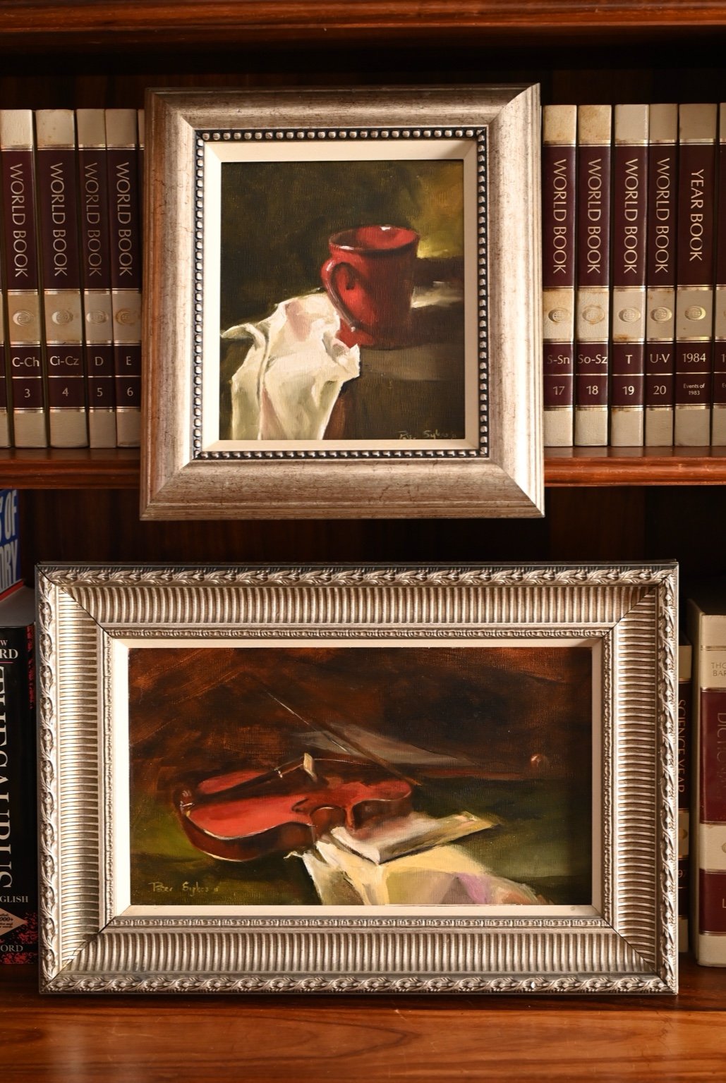 A beautifully paired set of still life oil paintings featuring a rich reg mug and a resting violin