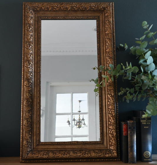 This vintage rectangular mirror is framed in classic gilded wood, featuring tiered moulding and embossed leaf motif along the border.