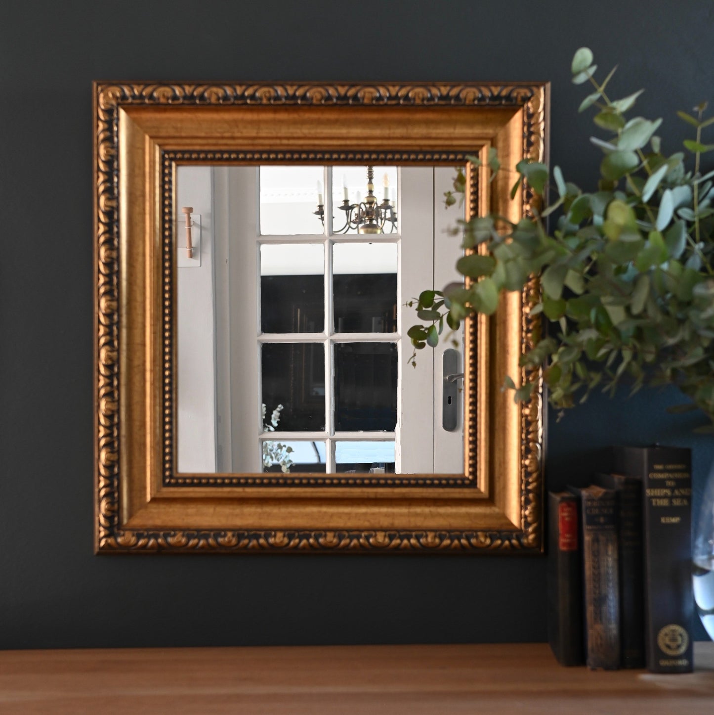 This vintage mirror features a classic gilded frame with layered moulding, beaded detail, and an embossed decorated border