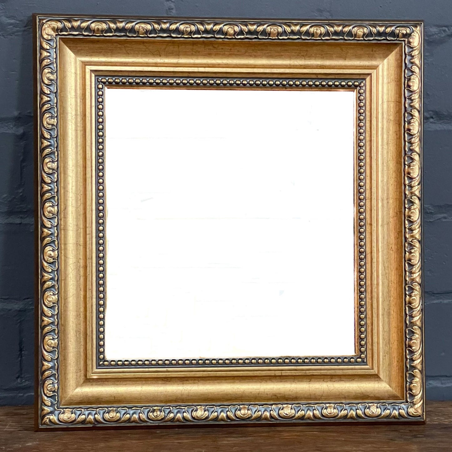 This vintage mirror features a classic gilded frame with layered moulding, beaded detail, and an embossed decorated border