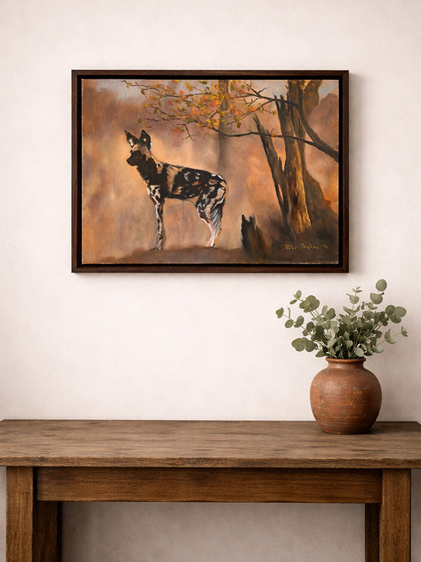 Framed painting of an African wild dog in an autumn forest above a wooden table with a vase of flowers.