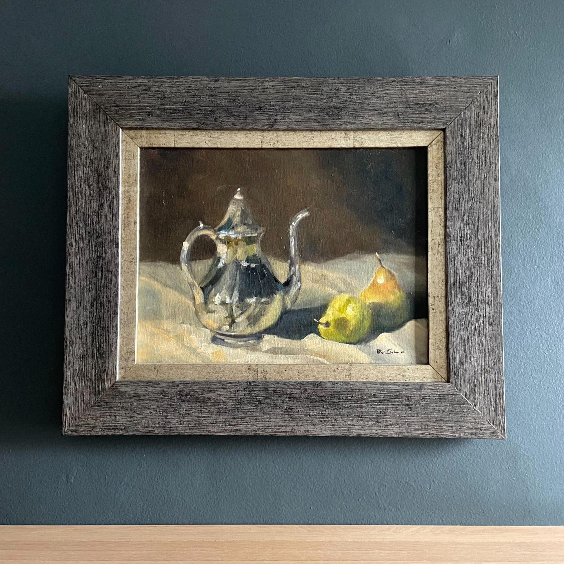 Beautiful oil painting of a silver coffee pot styled next to two pears on a tablecloth, framed in gold edging and a wooden frame.