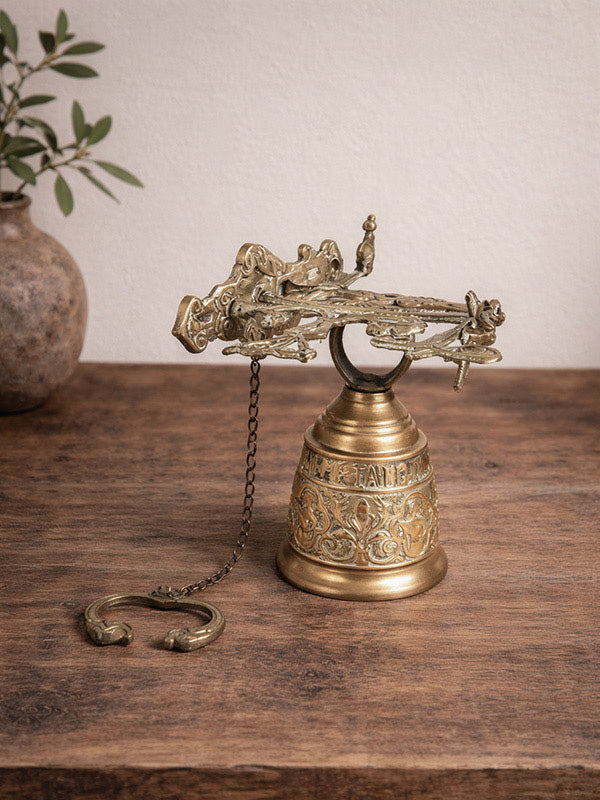 Decorative antique brass bell with intricate designs on a wooden surface.