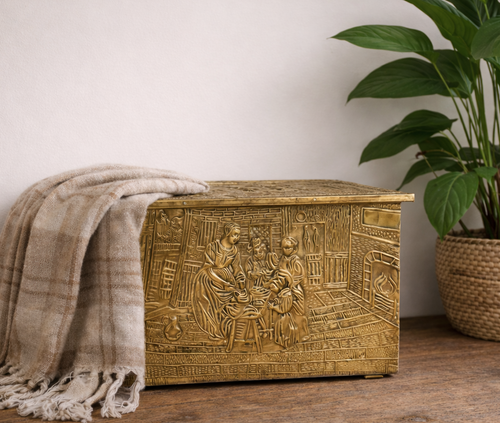 Decorative brass box with intricate designs on a wooden surface next to a plant.