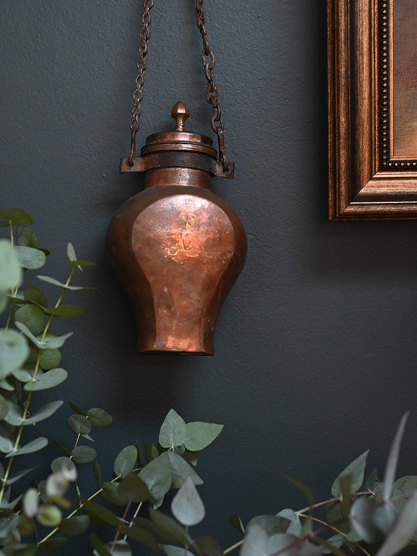 Antique copper water canteen on a dark wall with greenery and an antique painting