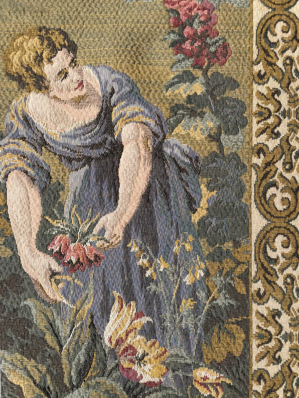 Tapestry of a woman in a blue dress holding flowers, surrounded by floral patterns.