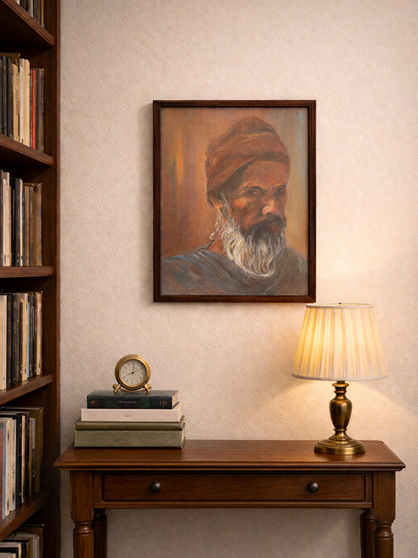 Framed portrait of a man with a turban above a wooden table with a lamp and books.