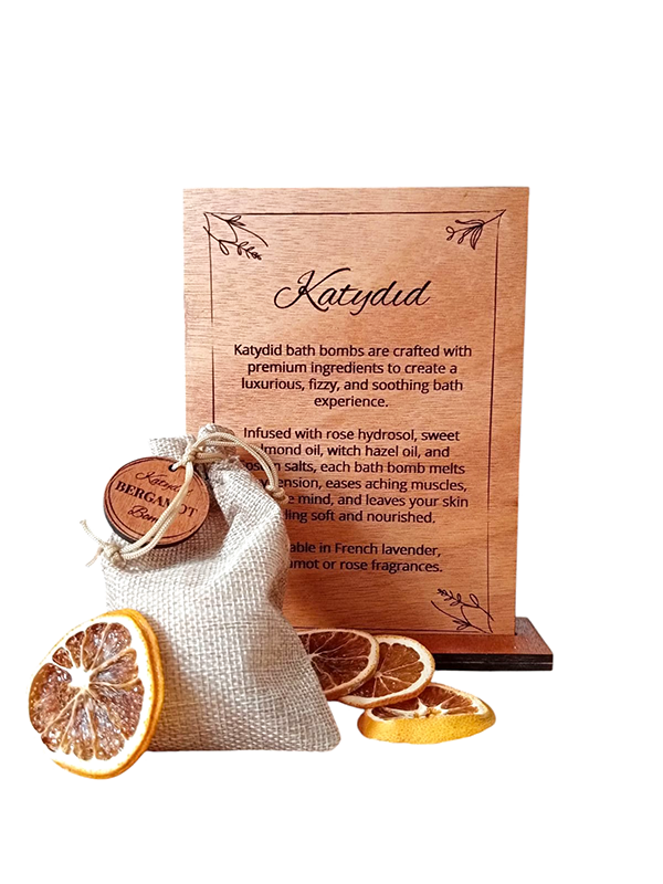 Katydid bath bomb packaging with wooden box and dried orange slices on a white background