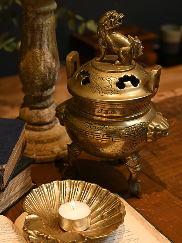 Decorative brass vintage foo dog incense burner with a candle on a wooden surface