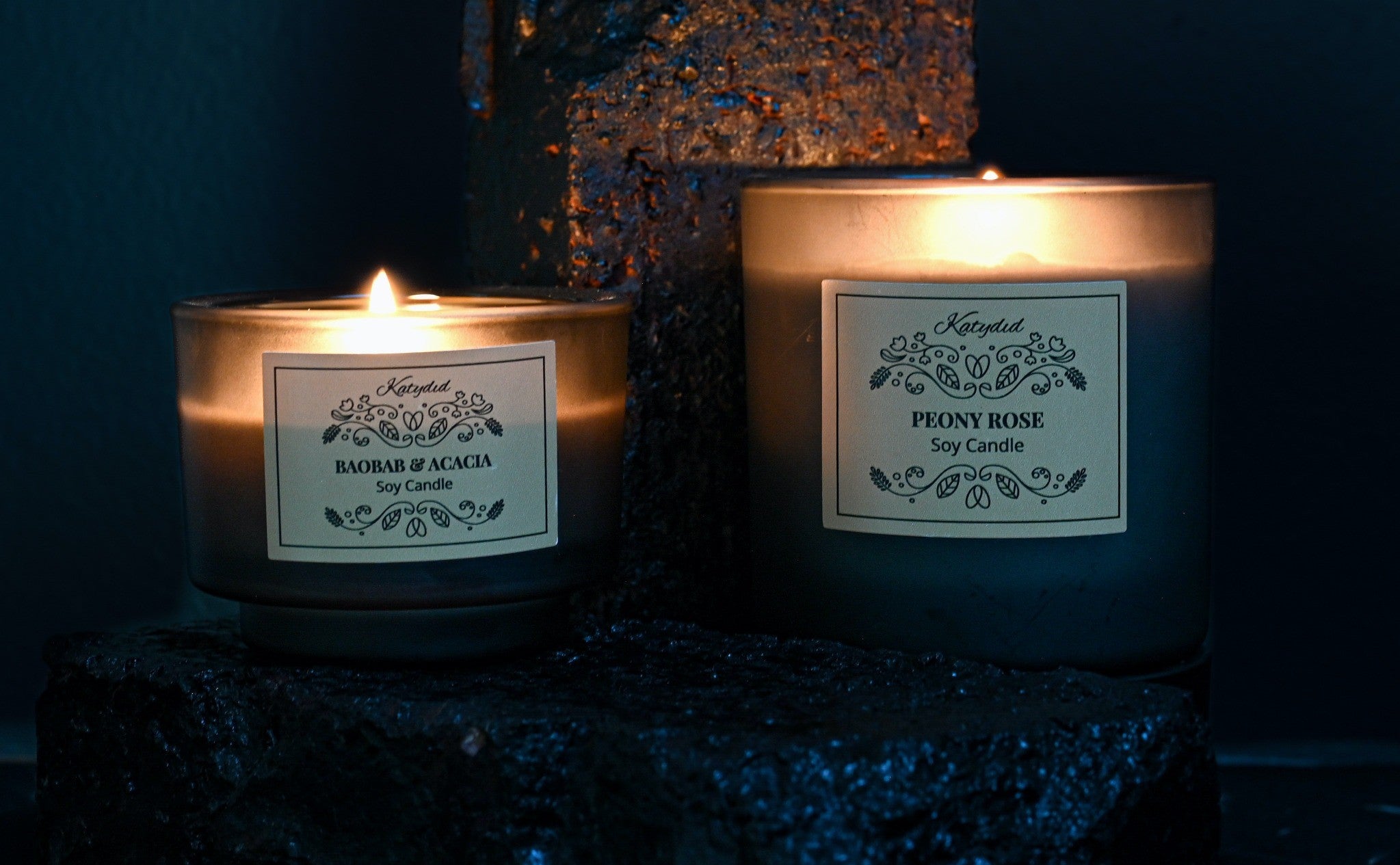 Two lit candles with labels on a dark background