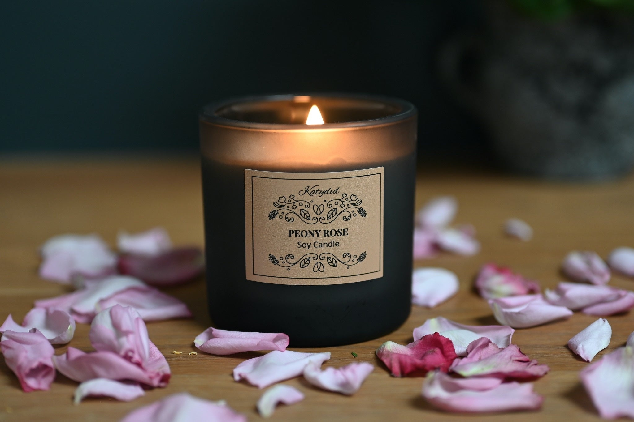 Candle with a label on a wooden surface surrounded by pink petals