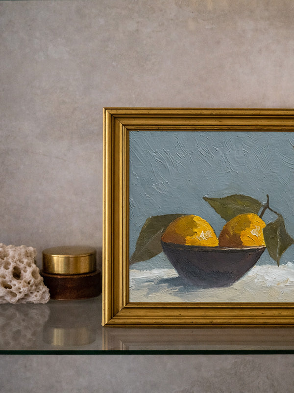 Framed still life painting of lemons in a bowl on a textured surface.