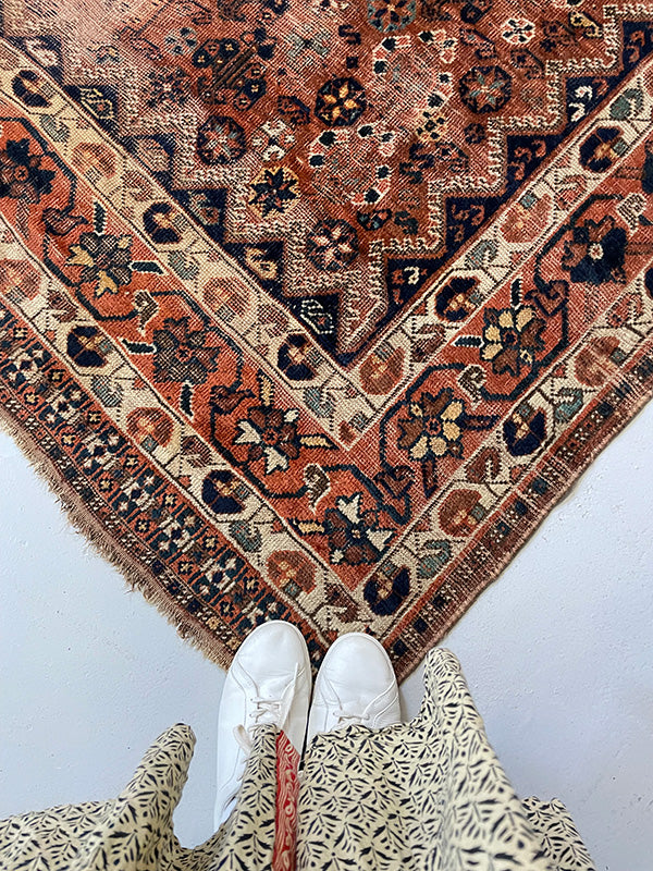 Patterned rug on a light gray floor with white shoes and a patterned garment.
