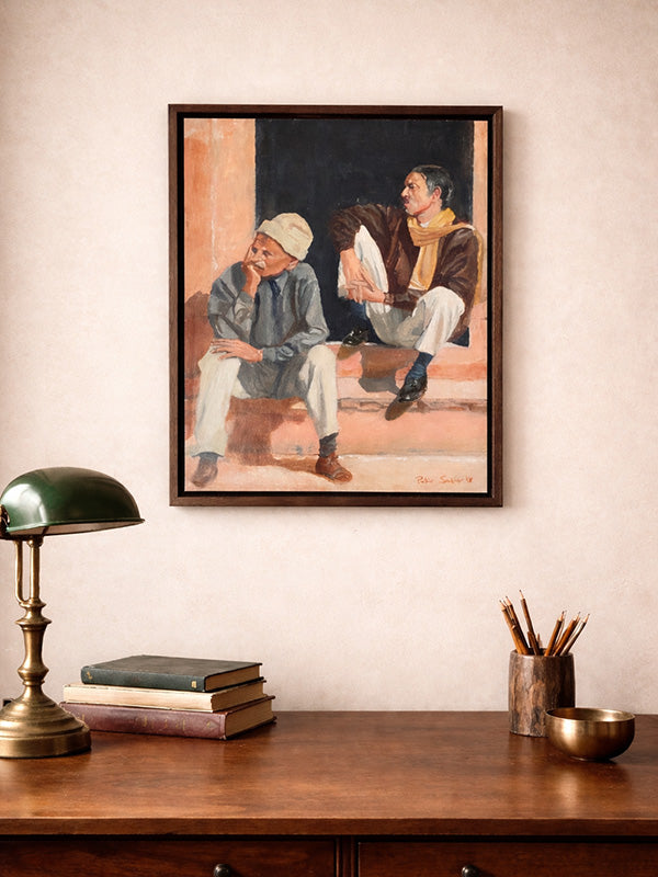 Framed artwork of two people on a wall above a wooden desk with books and a lamp.