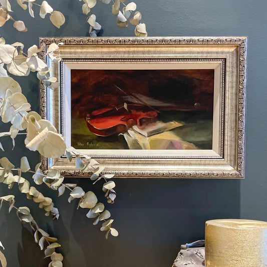 Framed painting of a violin on a dark wall with decorative leaves.