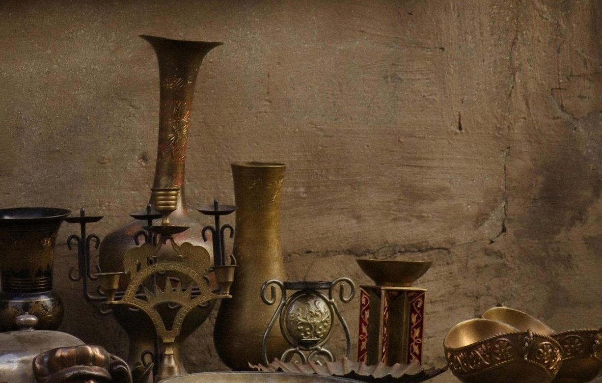 Collection of decorative metal vases and sculptures against a textured wall.