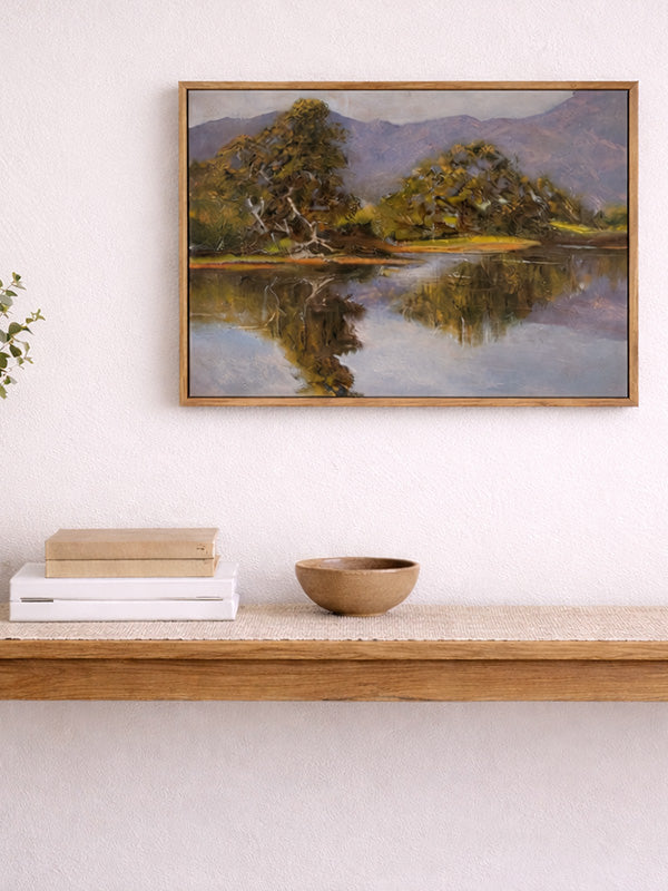 Framed landscape painting above a wooden shelf with books and a bowl.