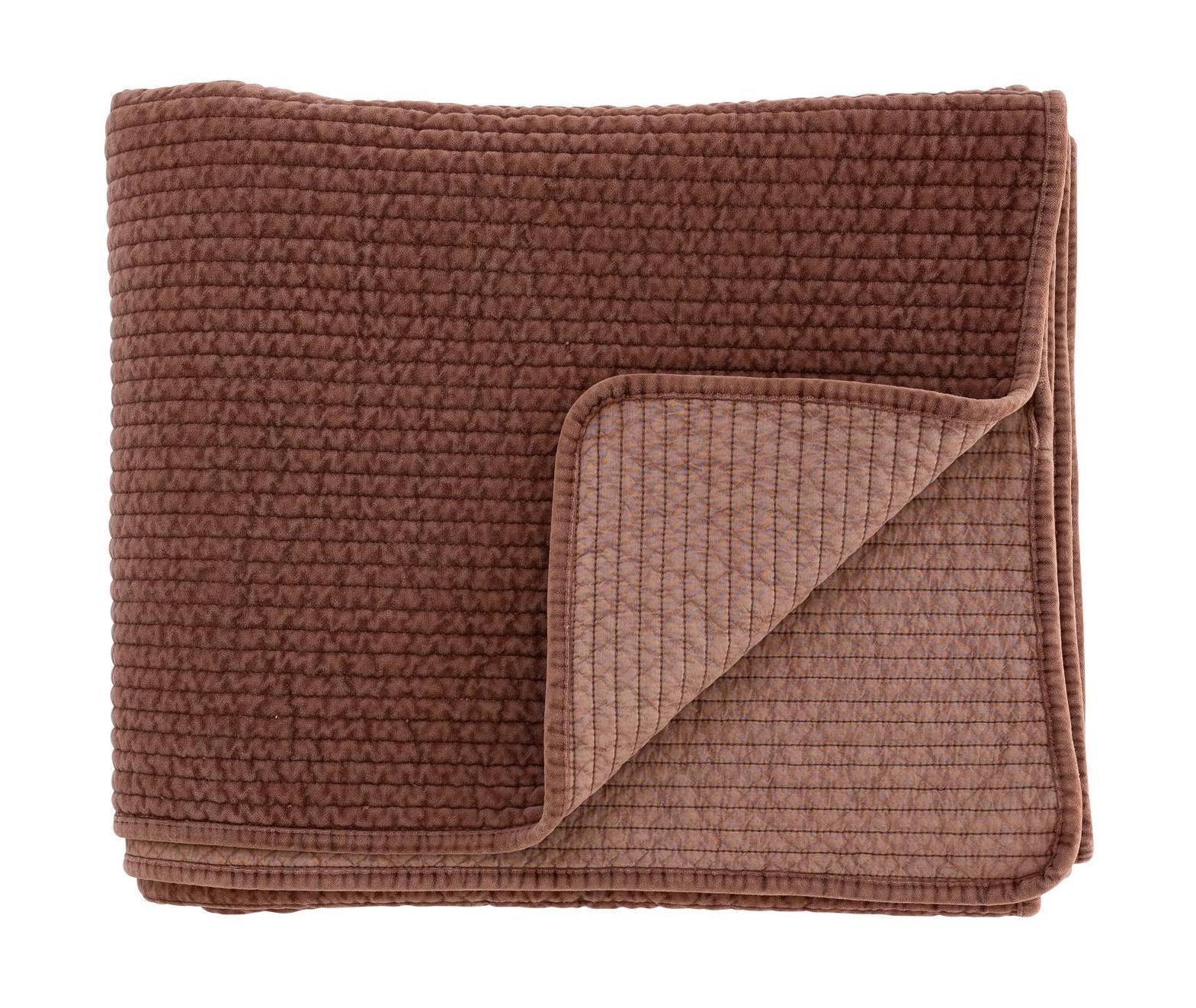 Folded rust coloured textured quilt on a white background