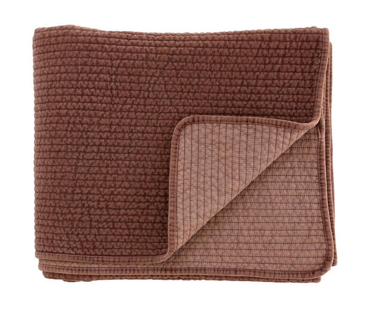 Folded rust coloured textured quilt on a white background