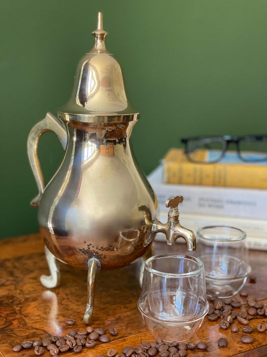 A vintage brass Samovar displayed on an antique walnut table with modern books, glass cups and coffee beans for decoration