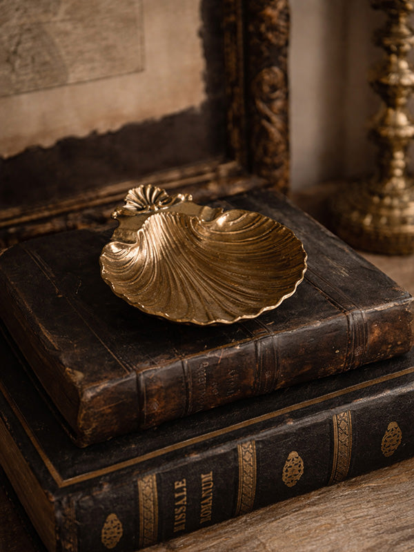 Vintage decorative brass shell shaped dish on a stack of old books with a blurred background