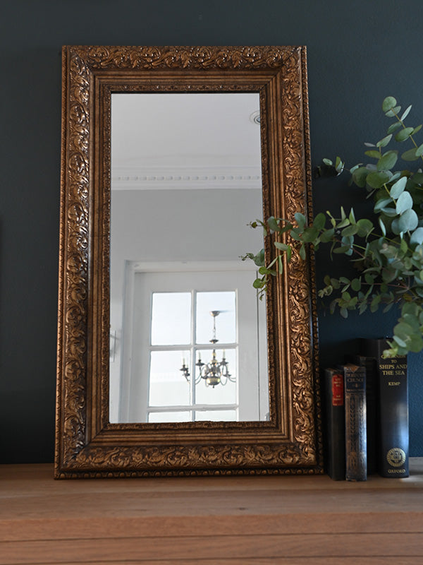 Decorative gold-framed mirror on a wooden surface with a dark wall background