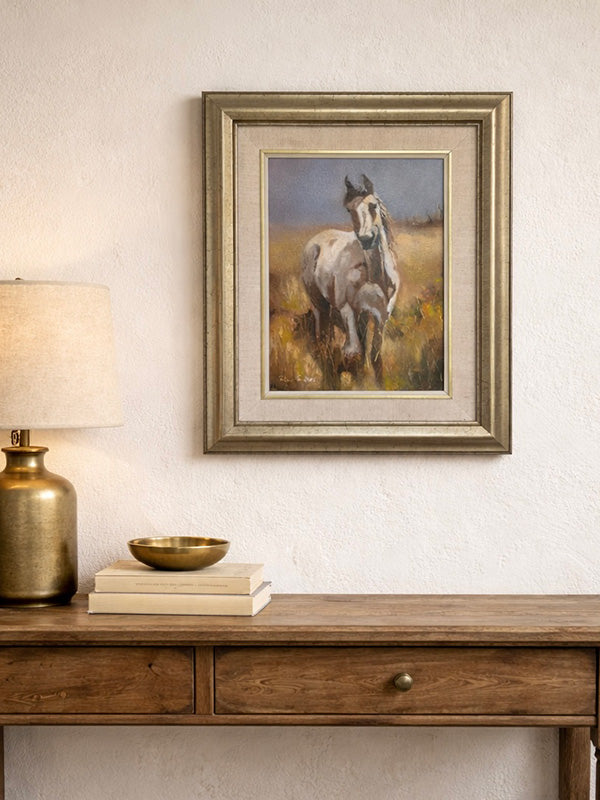 Framed painting of a horse on a wall above a wooden console table with decor items.